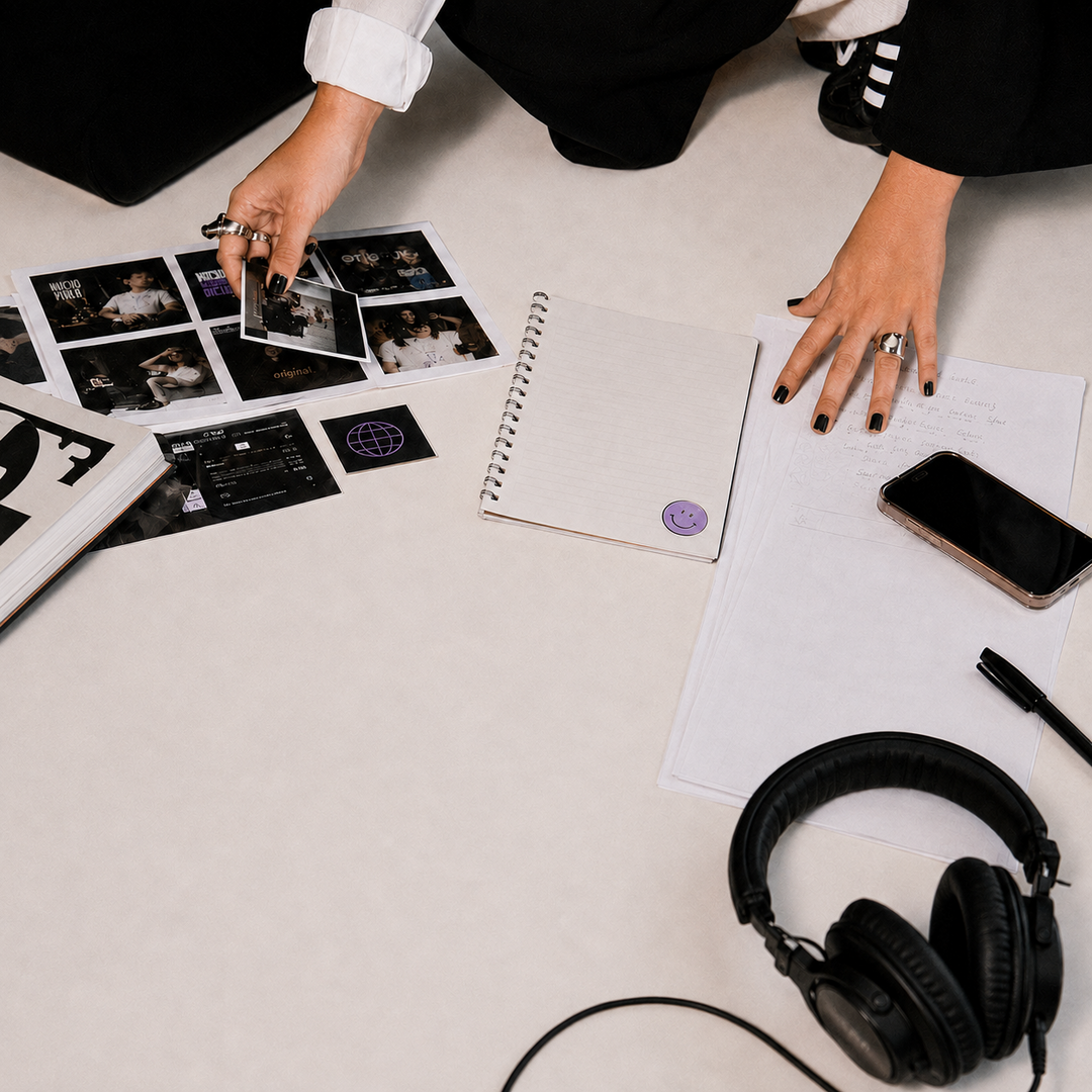 Mesa de trabajo creativo con cuaderno, referencias visuales, teléfono y audífonos